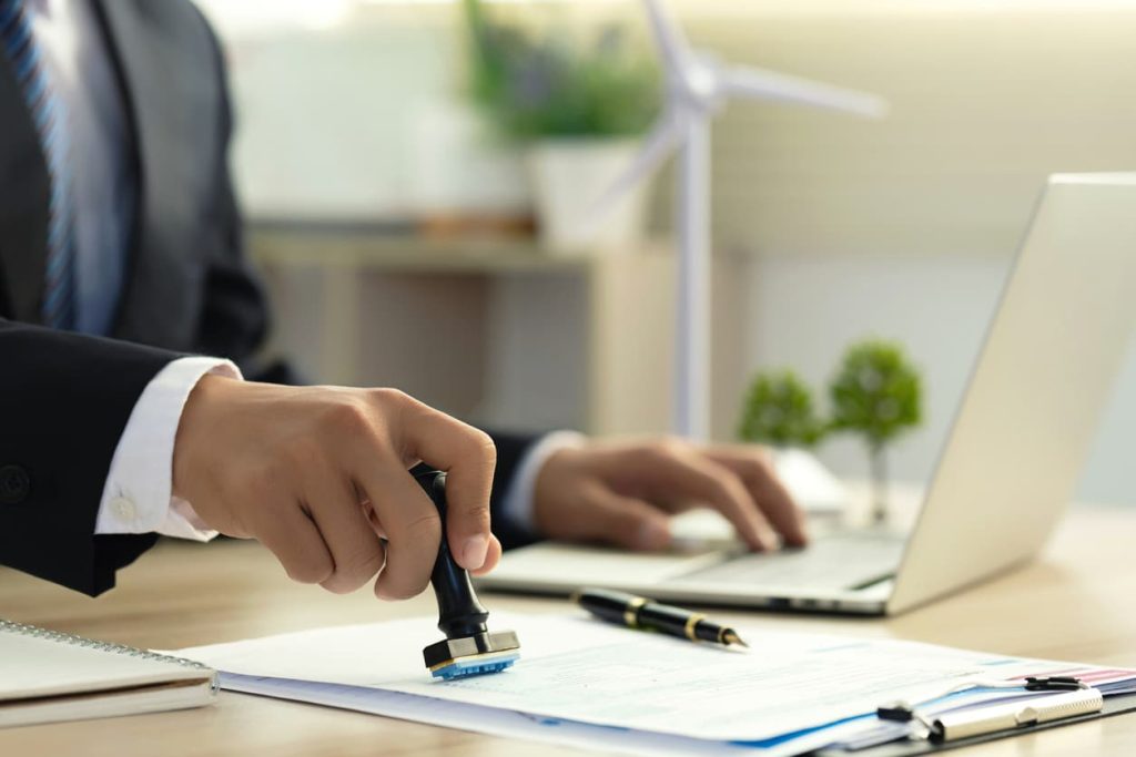 Close-up of professional using a stamp to certify a document at a desk, with a laptop and pen in the background.