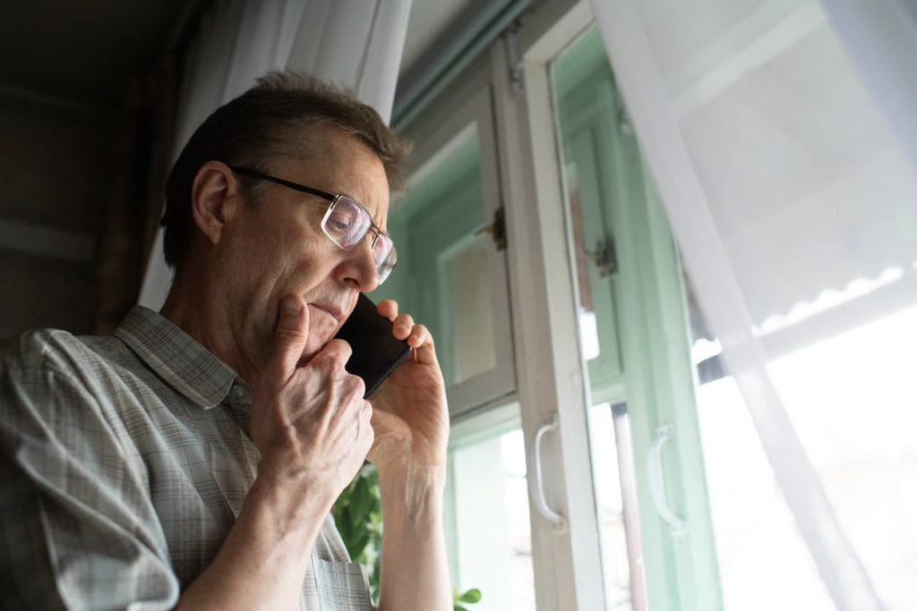 Concerned man on phone near window, symbolizing the importance of notary publics in fraud prevention and verifying identity at NotaryPublic24