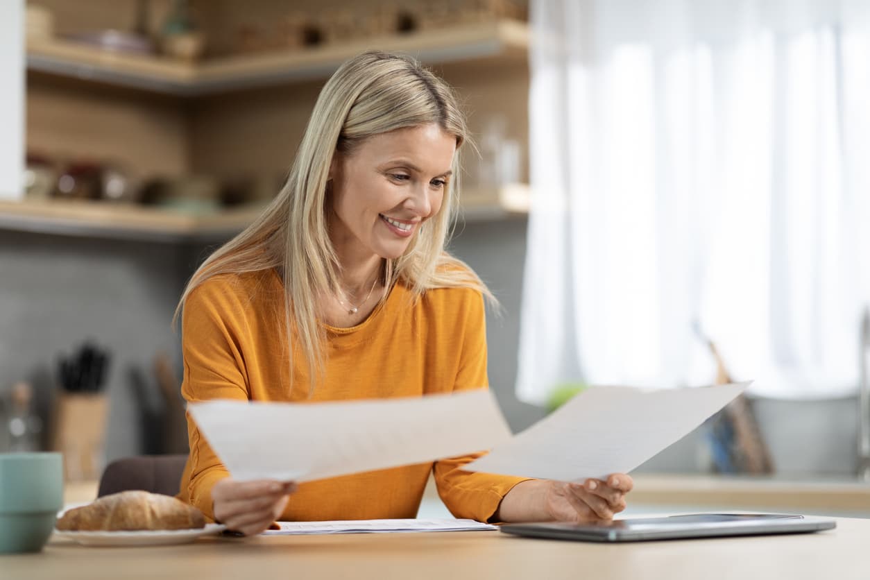 Smiling woman reviewing official documents at home – understanding proof of settlement and getting it notarized or Apostilled with NotaryPublic24.com